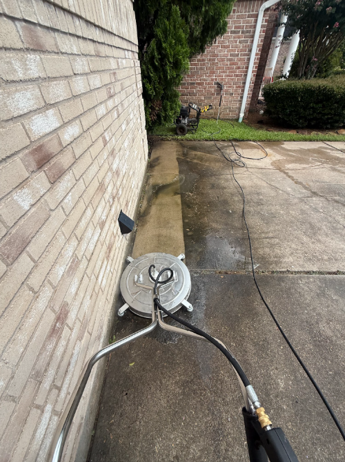 Surface cleaner washing a concrete driveway along a brick house